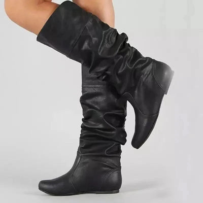 Women's black leather slouch knee-high boots with high heels, shown worn on a model's leg, highlighting the fashion design and leather texture.